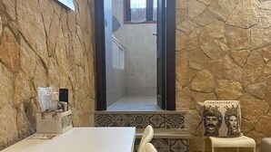 Une pièce avec un mur en pierre, une table blanche, une chaise et une petite table sur laquelle se trouve un objet décoratif.