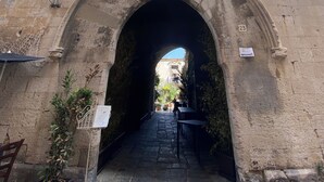 Une entrée en arc donnant sur un bâtiment à la façade en pierre, avec un petit balcon et une fenêtre située au-dessus de l’arc.