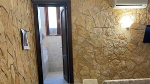 Une pièce avec un mur en pierre, une table blanche avec une chaise, un canapé et un petit escalier menant à une autre pièce.