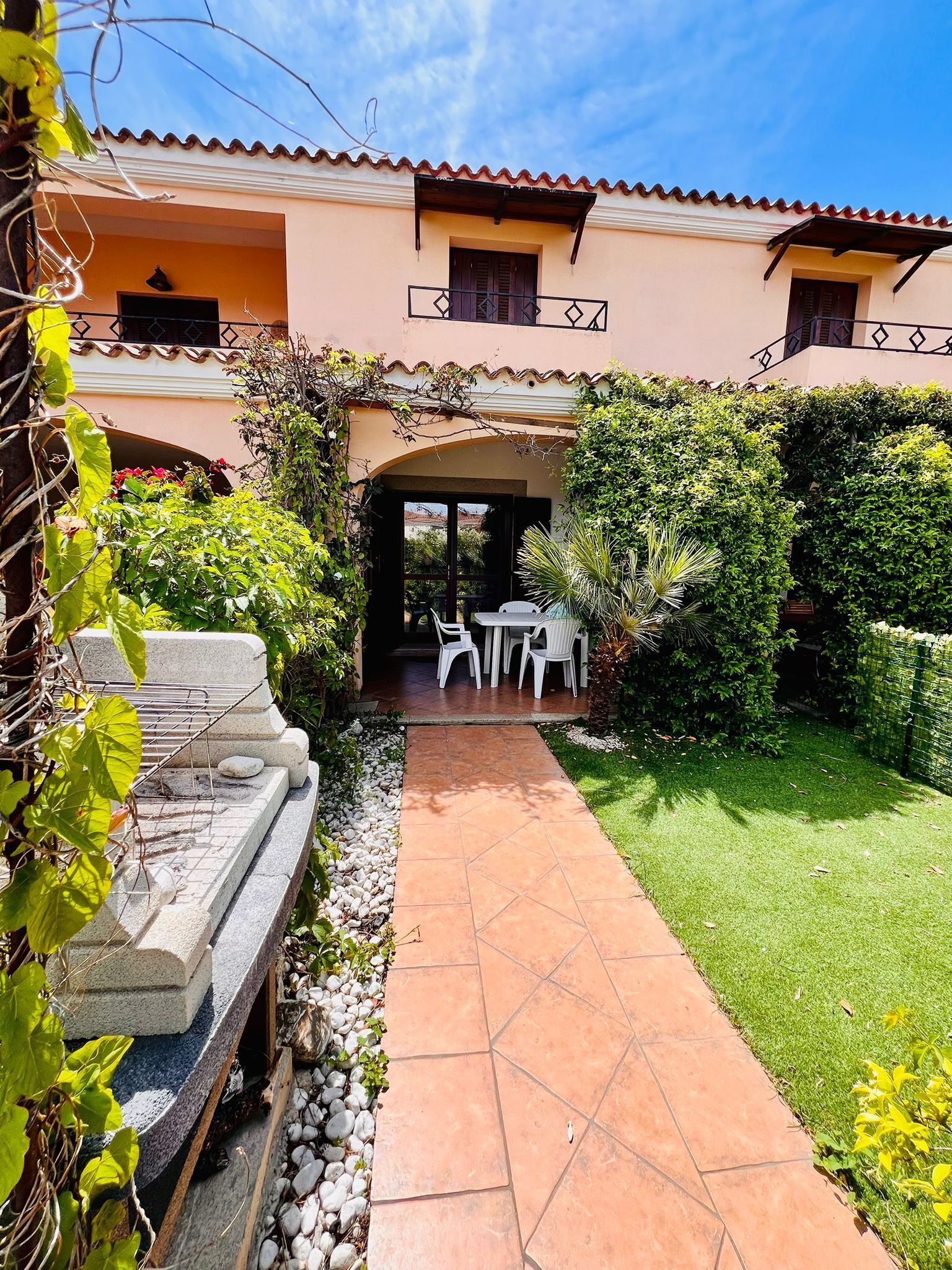 Ein Patio mit einem gepflasterten Weg, der zu einer Sitzgruppe mit weißen Stühlen und einem Tisch führt.