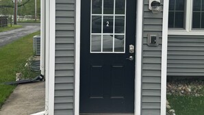 Une maison d'habitation avec une porte d'entrée noire, un petit porche et le numéro « 2 » sur la porte.