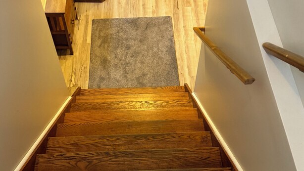 Un escalier en bois avec une rampe, menant à un palier recouvert d’un tapis gris.