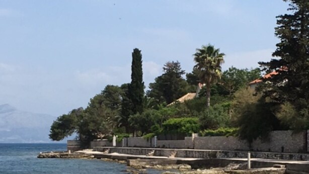 A coastal walkway with a pebble path leading to a beach, surrounded by trees and a stone wall. - S&A Apartment (Sutivan)