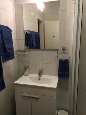 A bathroom with a white sink, a mirror, and a glass shower enclosure. - S&A Apartment (Sutivan)