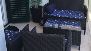 A balcony with wicker furniture, a potted plant, and a decorative wall hanging. - S&A Apartment (Sutivan)