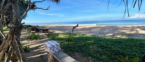 A beach with a wooden bench, lounge chairs, and a stack of towels.