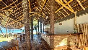Un restaurant situé en bord de mer, avec des meubles en bois et un plafond en bambou.