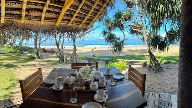 Une table en bois, dressée pour le repas, avec vue sur la plage et l’océan.