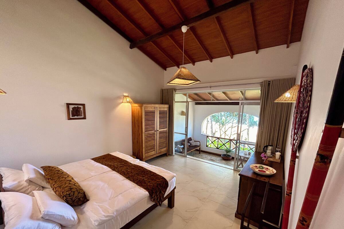 Ein Schlafzimmer mit Bett, Kleiderschrank, Schreibtisch und Stuhl sowie Blick ins Freie.