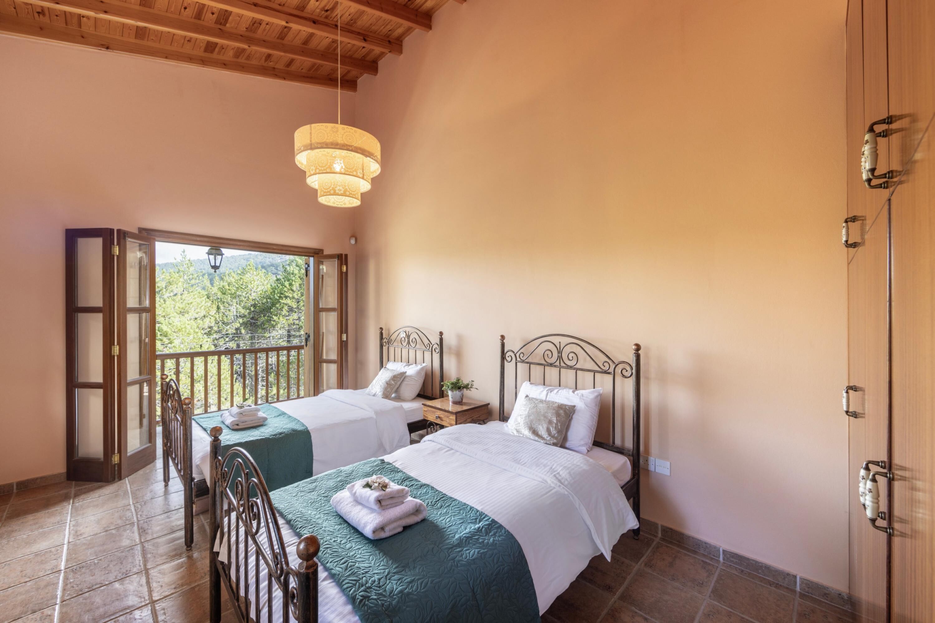 A room with two beds, a balcony, and a view of greenery outside.