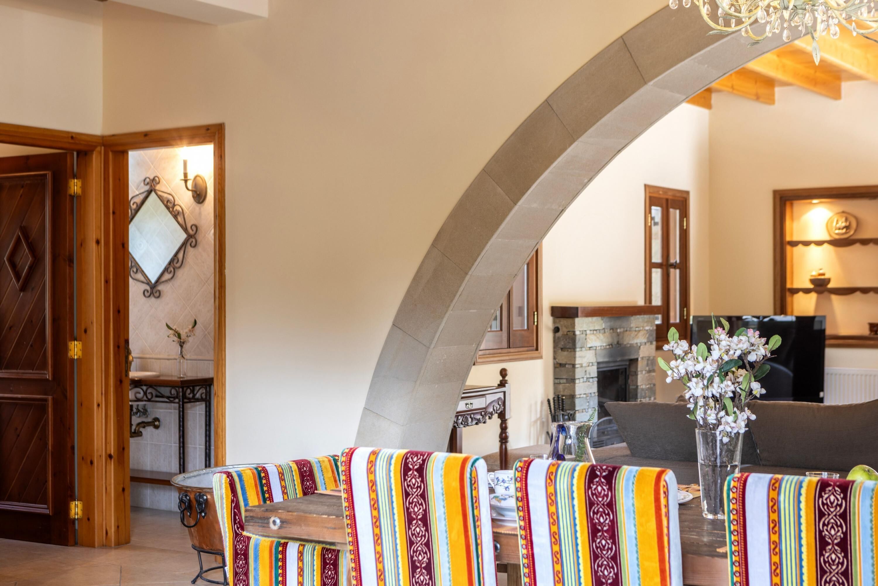A dining area with a wooden table and chairs, a chandelier, and a stone archway.