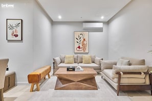 Relax in a serene space with a beige sofa, wooden bench, and coffee table, surrounded by abstract art and a stylized print.