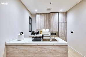 Kitchen features a large island with a sink and a dish rack, along with a coffee machine and stainless steel refrigerator.