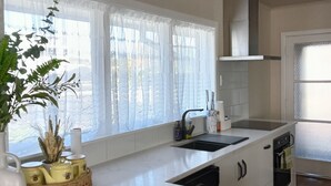 A modern kitchen with white marble countertops, a built-in oven, and a large window with sheer curtains. - Steam land stay  (Rotorua)