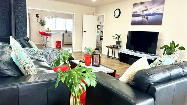 A living room with a black leather sofa, a flat-screen TV, and a dining area with a white table and chairs. - Steam land stay  (Rotorua)