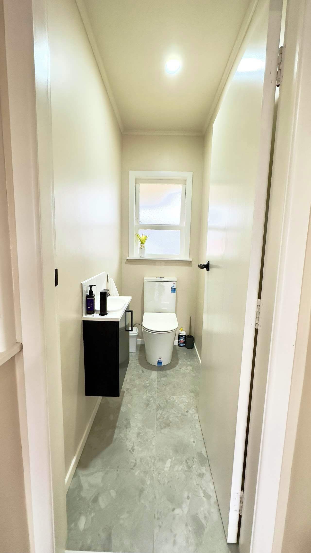 A narrow bathroom with a toilet, sink, and window.