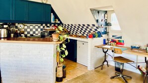 A compact kitchen with teal cabinets, a checkered backsplash, and a small dining area with a table and chair. - Charming flat under the roof (Paris)