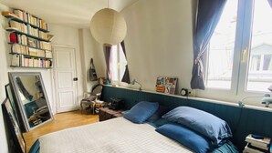 A bedroom with a bed, a bookshelf, a desk, and a window with curtains. - Charming flat under the roof (Paris)