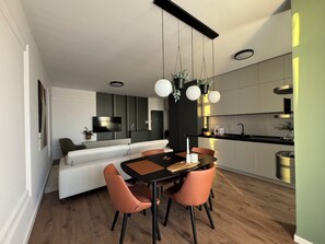 A modern kitchen with a dining area, featuring a black and white color scheme, wooden flooring, and pendant lighting. - Joy City Stay Nord One N2-49 (Timișoara)