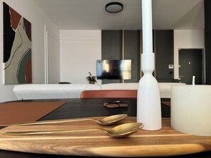 A modern hotel room with a wooden dining table, a white vase, and a flat-screen TV mounted on the wall. - Joy City Stay Nord One N2-49 (Timișoara)