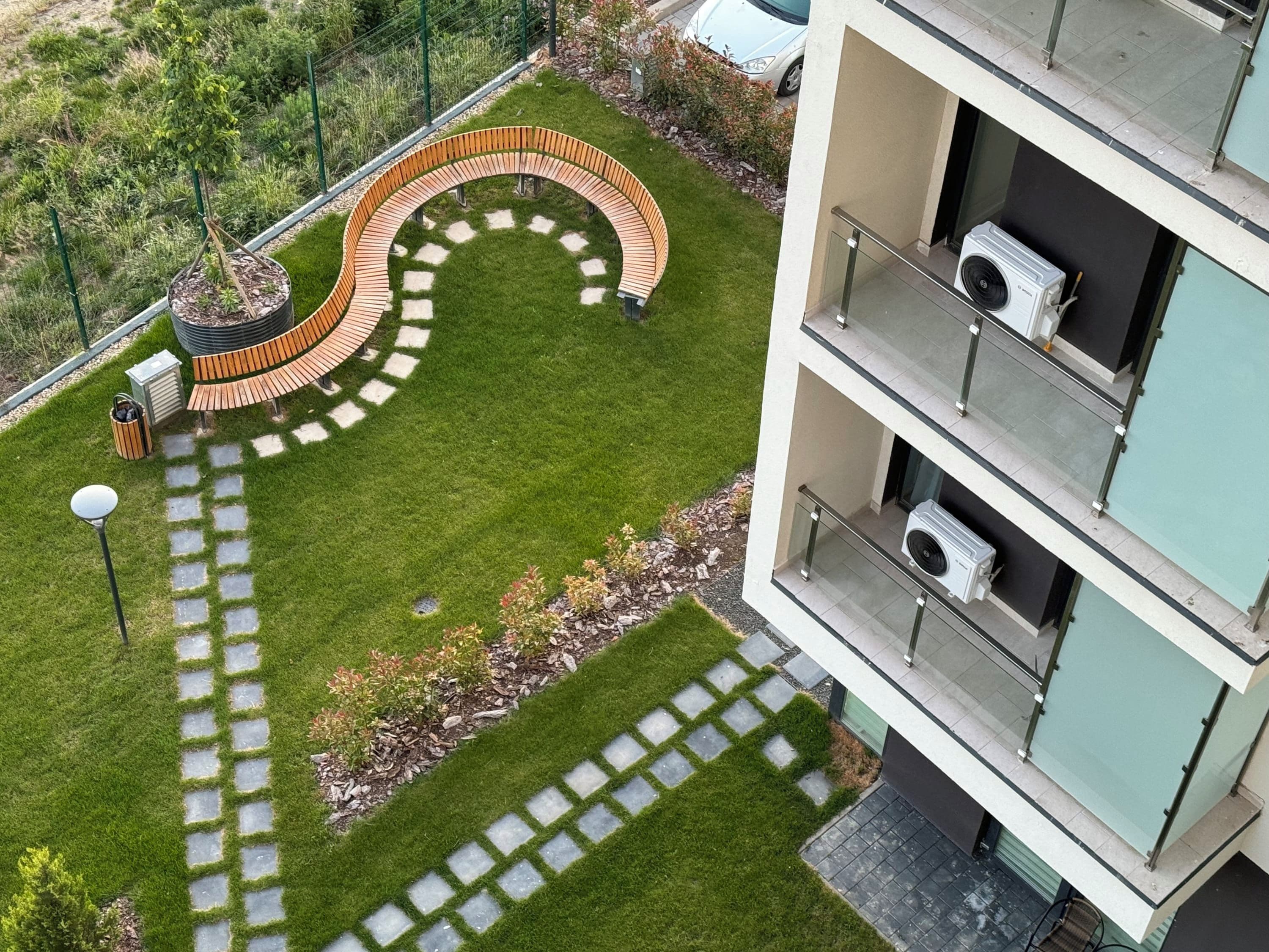 Un immeuble à plusieurs étages doté d’un espace extérieur aménagé en terrasse avec des assises incurvées, d’un chemin et d’un petit jardin.