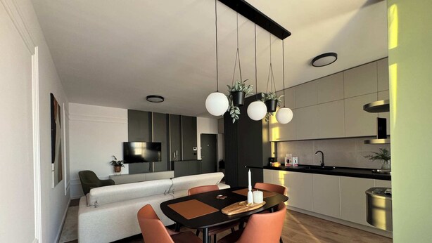 A modern kitchen with a dining area, featuring a wooden table, two chairs, and pendant lights. - Joy City Stay Nord One N2-49 (Timișoara)