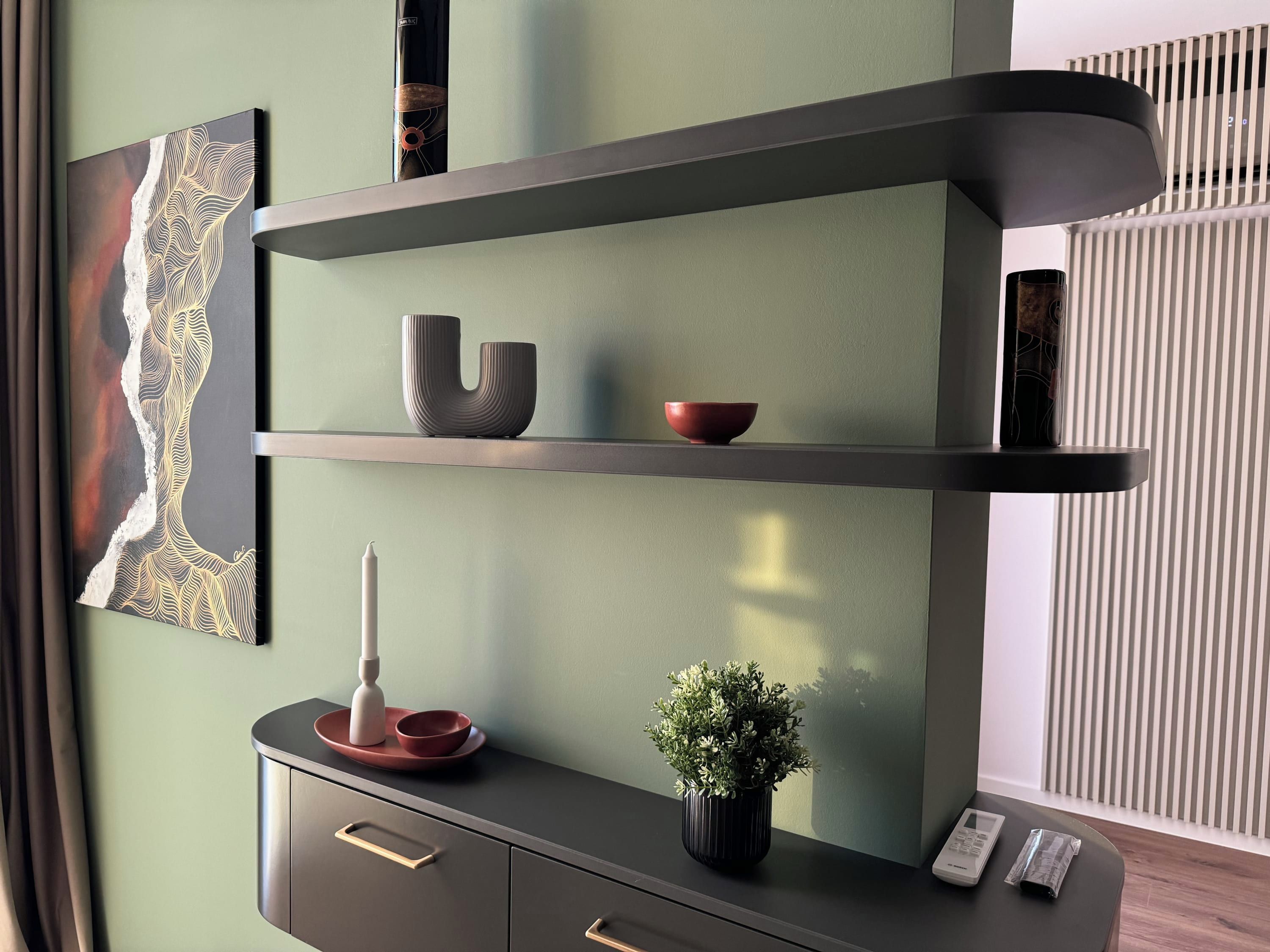 A modern interior with a dark-toned console table, a wall-mounted shelf with decorative items, and a potted plant.