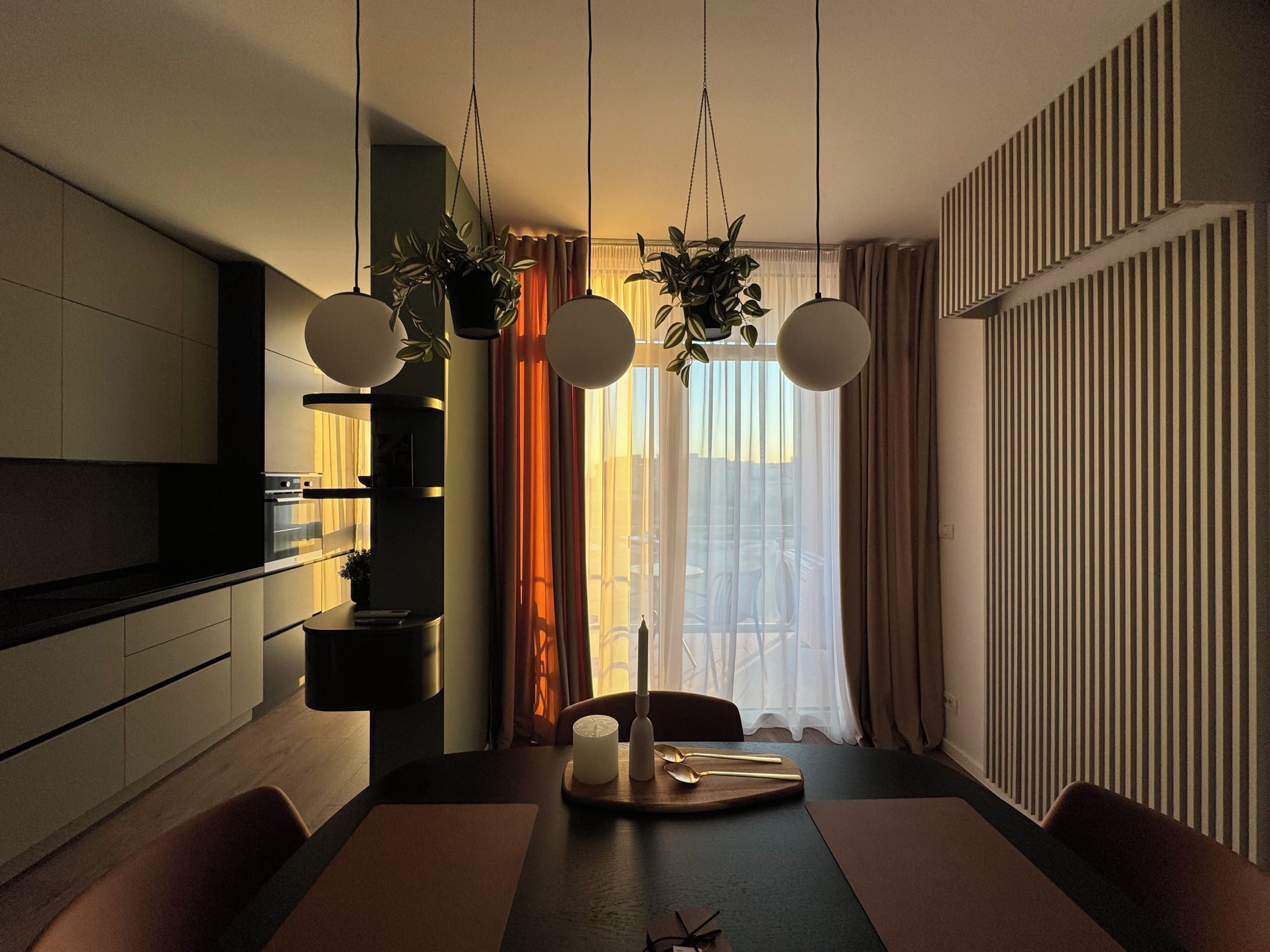Un espace de salle à manger moderne avec une longue table, des chaises, des plantes suspendues et des luminaires suspendus.