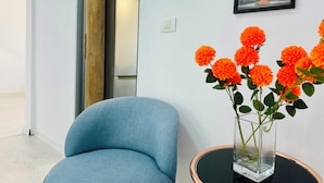 Una habitación moderna con un sillón azul, un florero de cristal con flores naranjas, un cuadro con la Torre Eiffel y una puerta de madera.