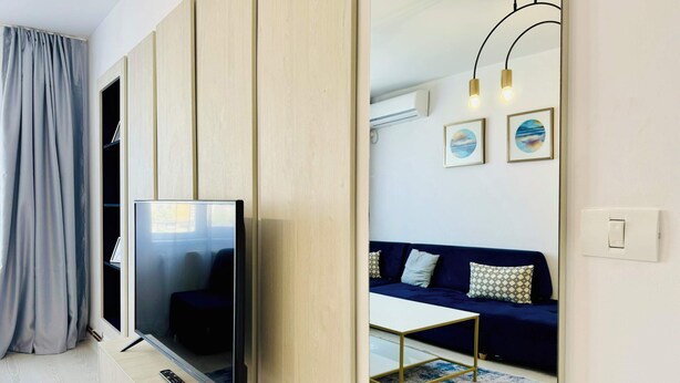 Una sala de estar moderna con un televisor de pantalla plana sobre un soporte de madera, un sofá con cojines estampados, una mesa de centro y una alfombra azul y blanca.