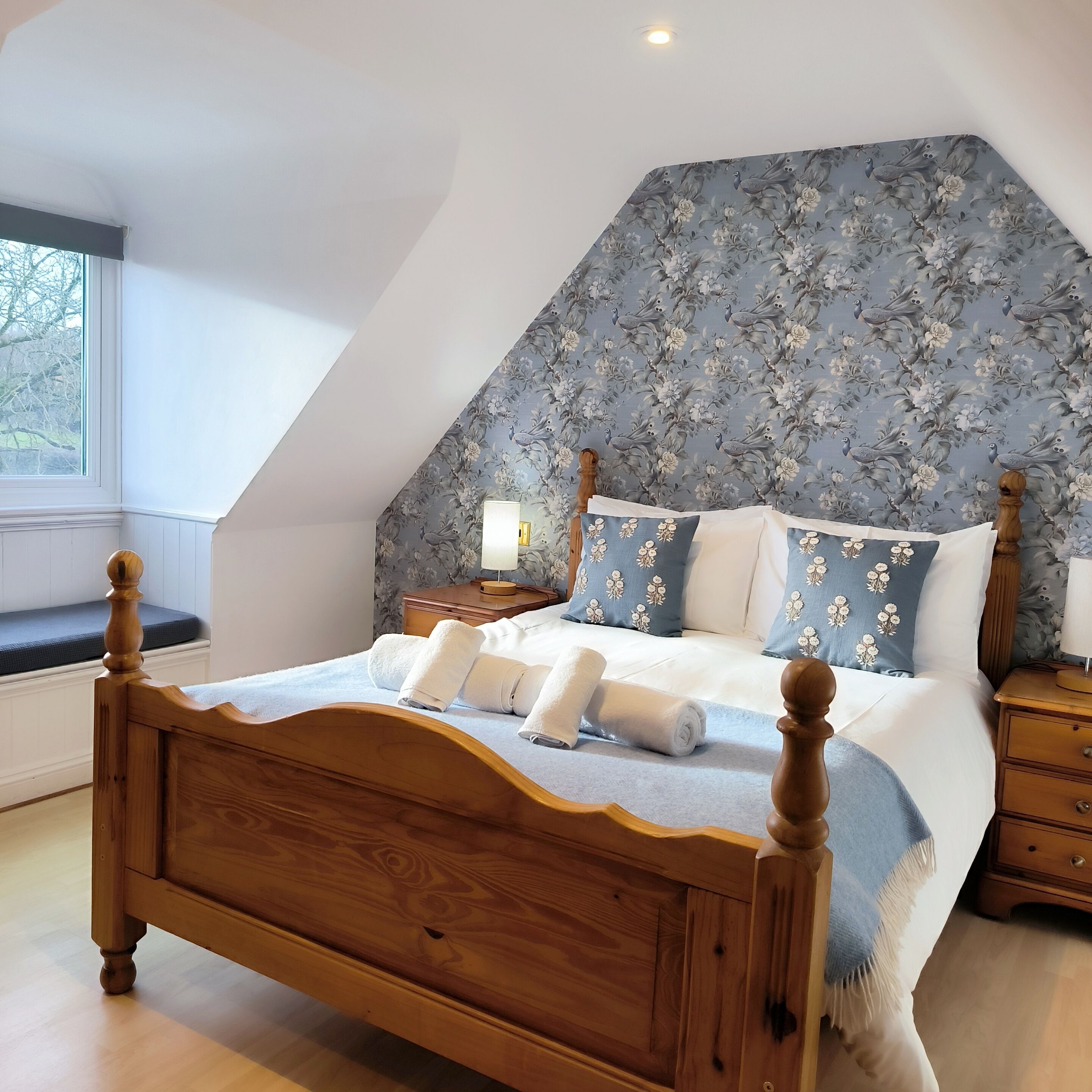 A bedroom with a sloped ceiling, a wooden bed frame, and floral-patterned headboard.