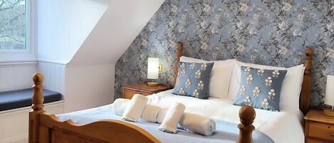 A bedroom with a sloped ceiling, a wooden bed frame, and floral-patterned headboard.