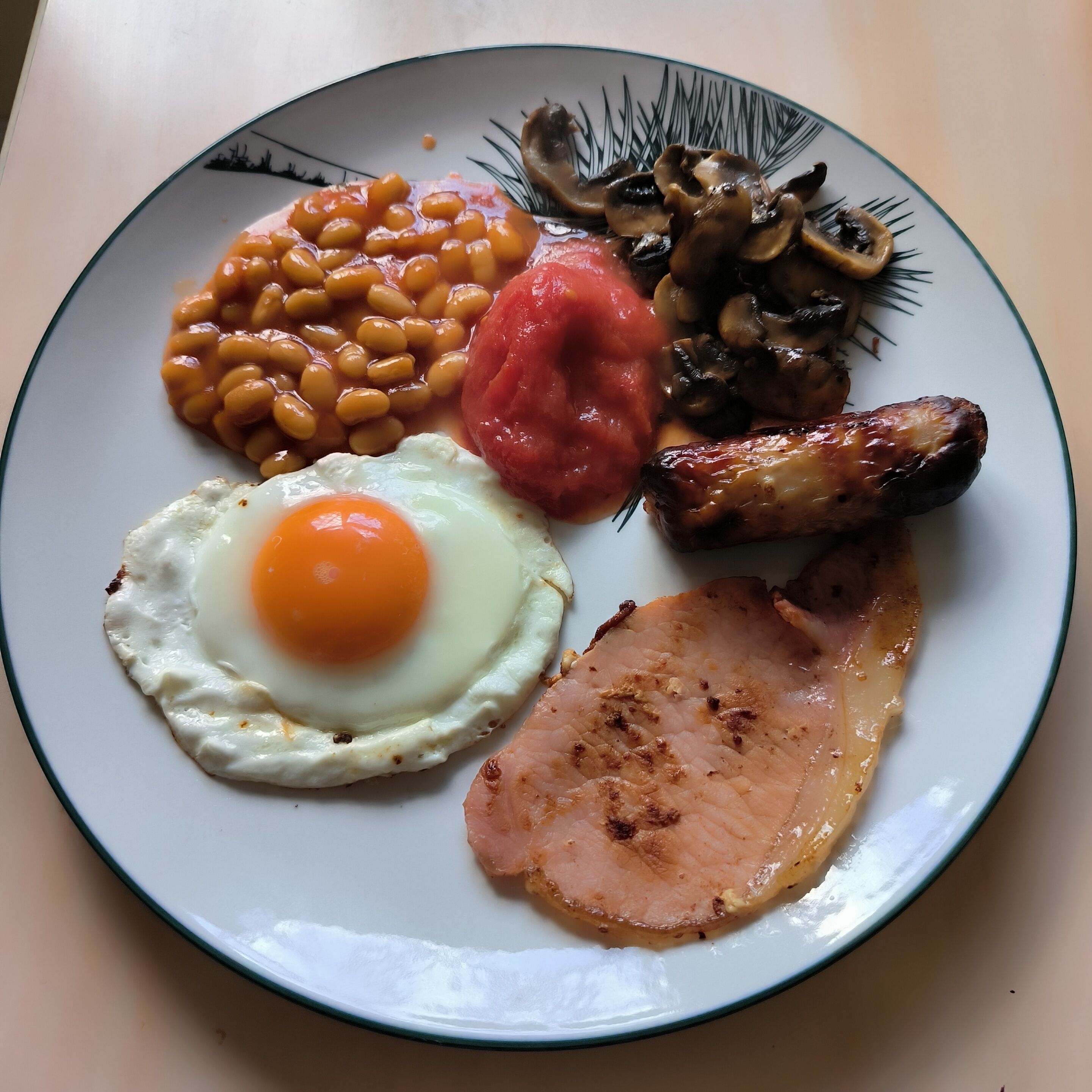 Ein Teller mit Frühstückspeisen, darunter Eier, Bohnen, Tomaten, Pilze und Schinken.