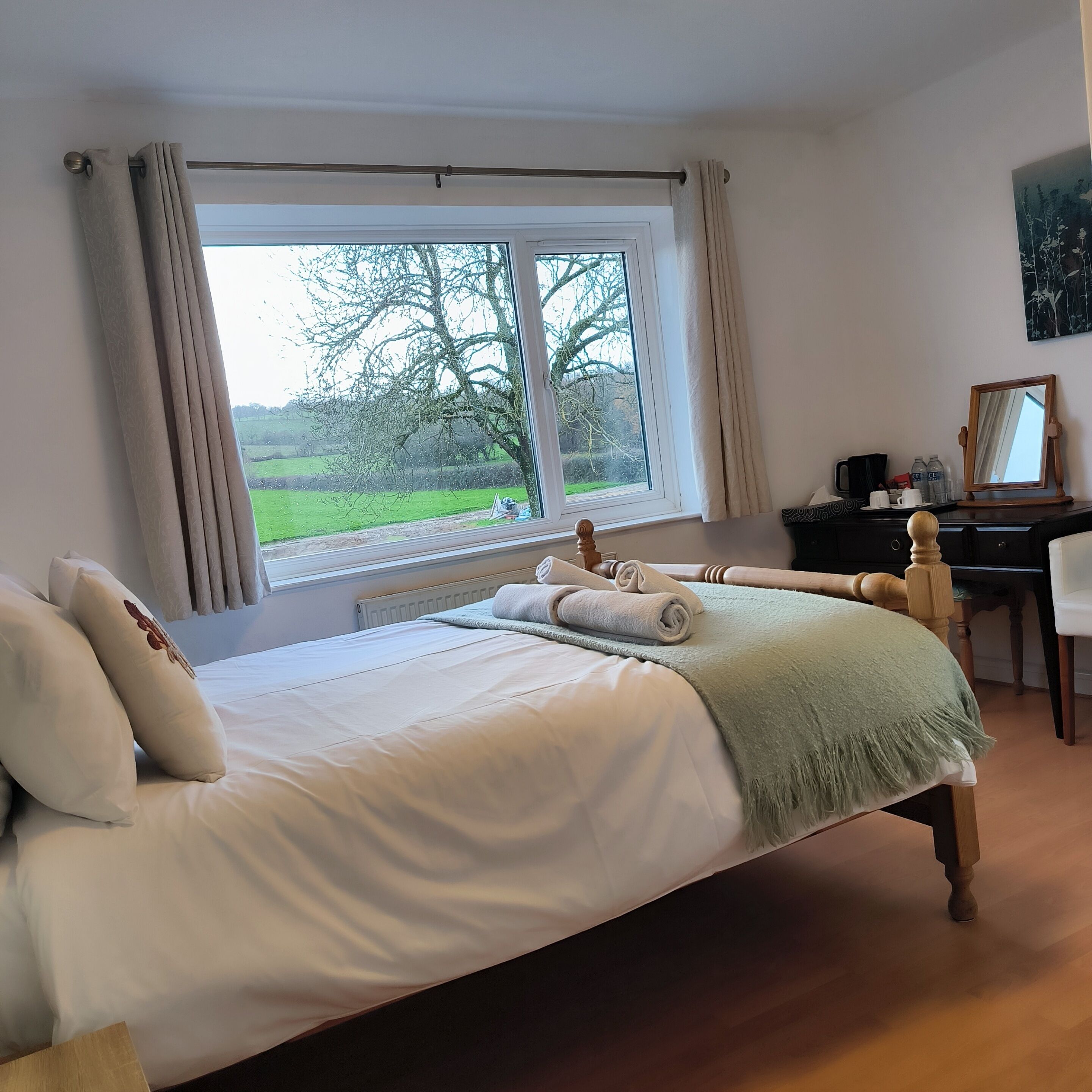 A bedroom with a large bed, a desk, and a window with a view of greenery.