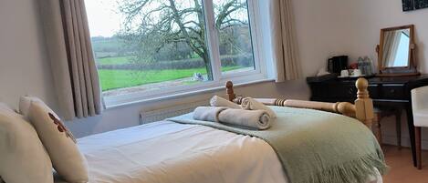A bedroom with a large bed, a desk, and a window with a view of greenery.