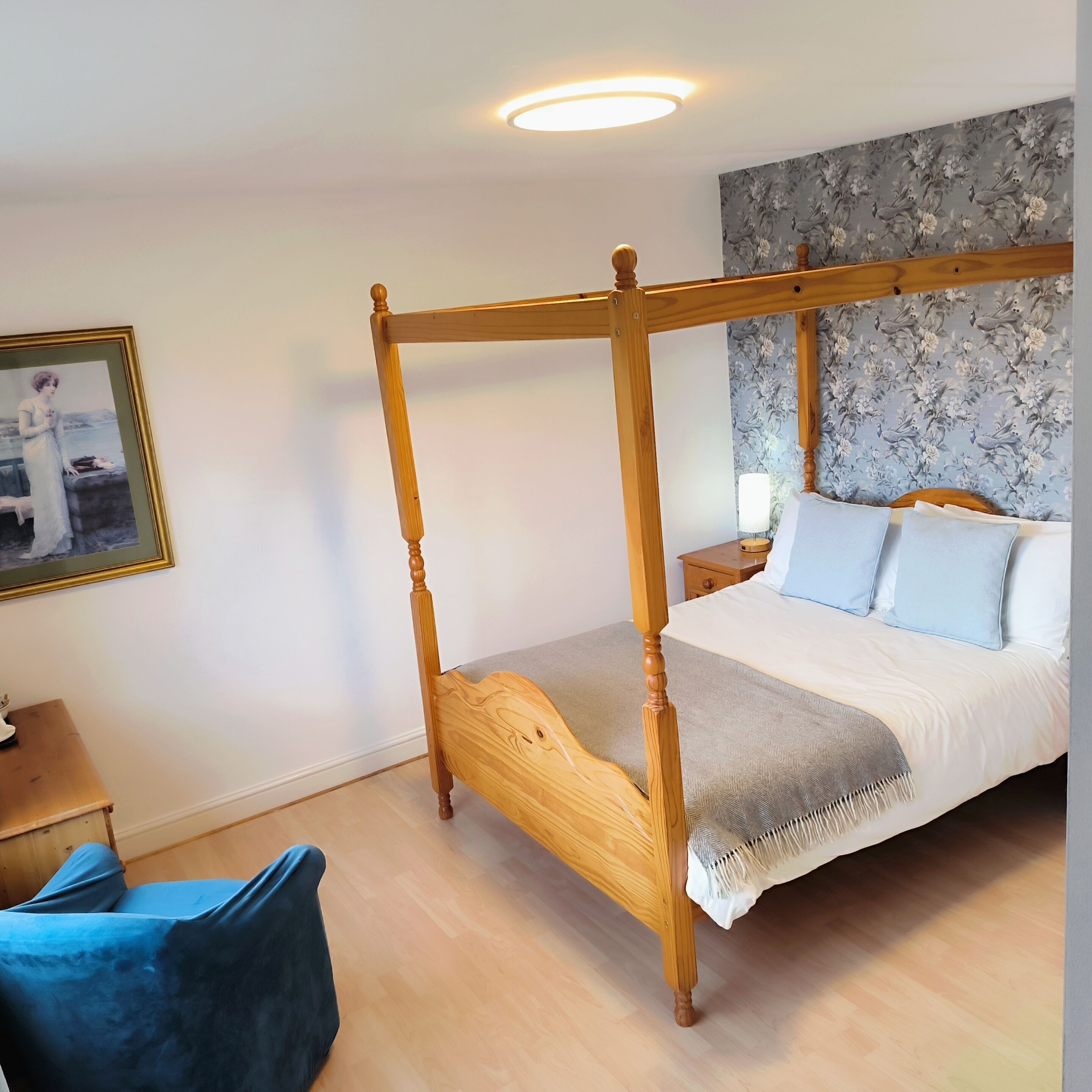 A four-poster bed with a wooden frame, a bedside table, a lamp, and a floral wallpaper.