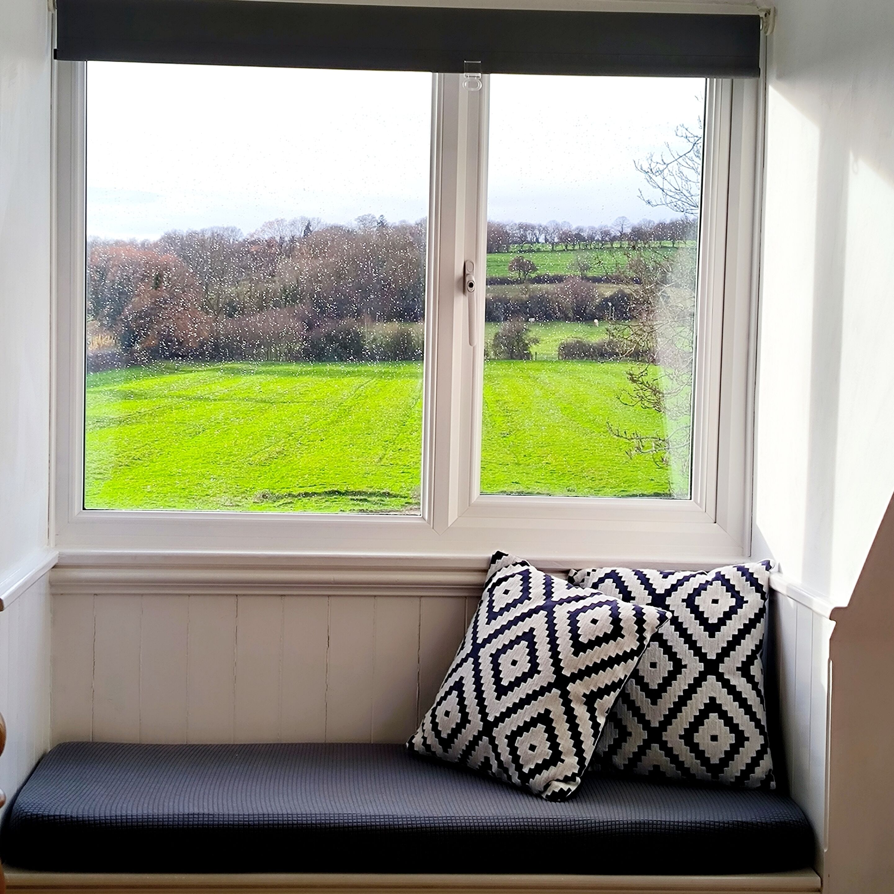 A window seat with a patterned cushion and a view of a green field.
