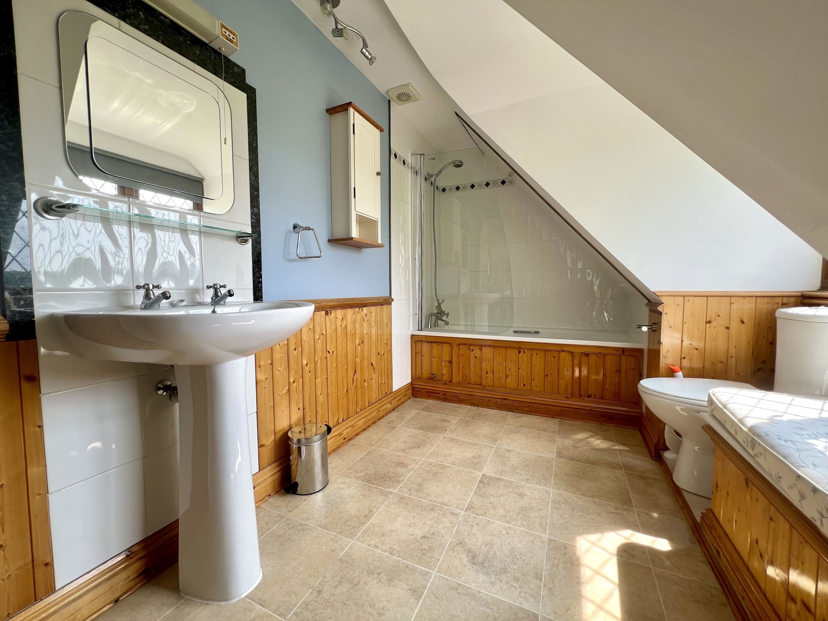 Een badkamer met een wastafel, toilet, douche en een houten opbergmeubel.