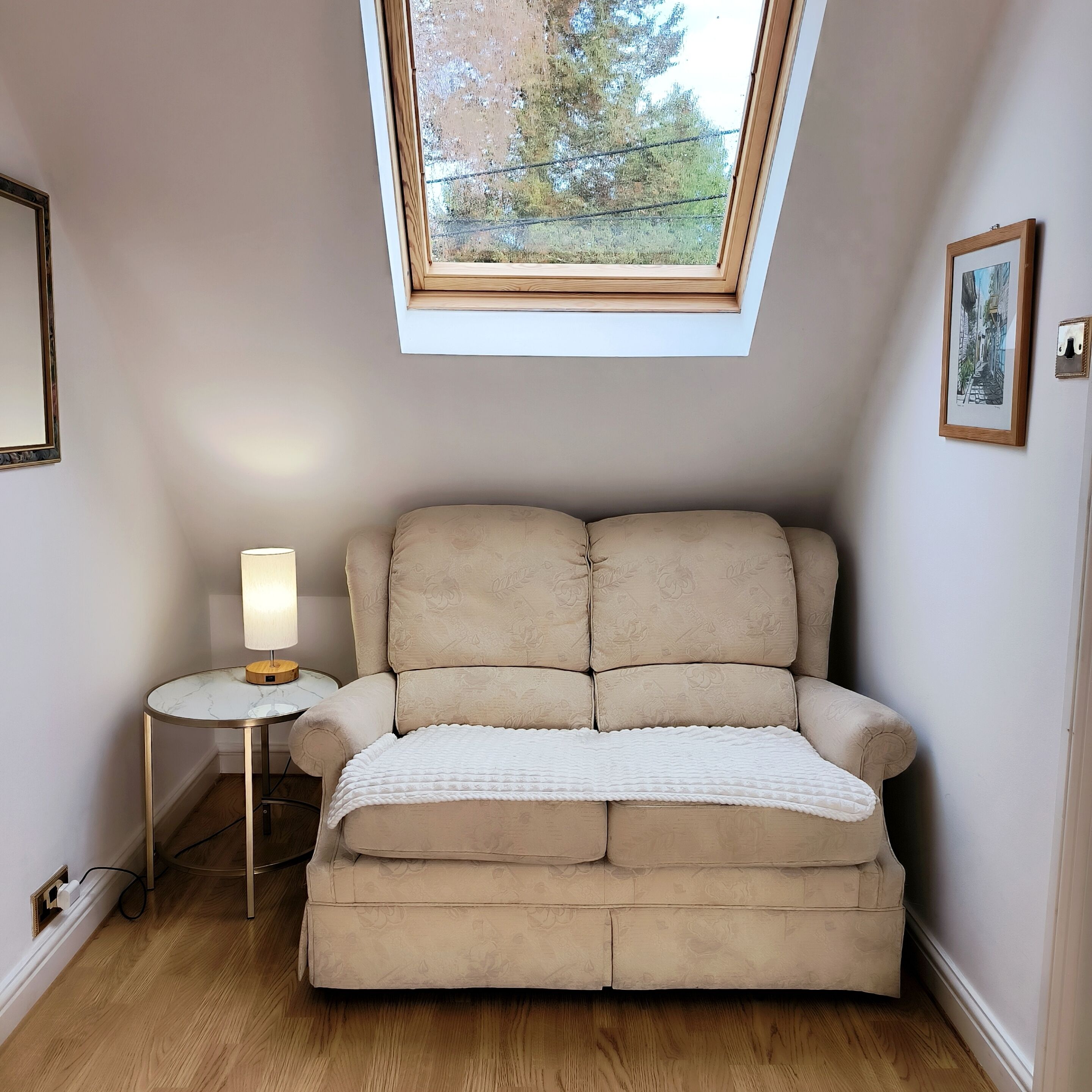 A cozy room with a sofa, a small side table, and a window with a view of trees.