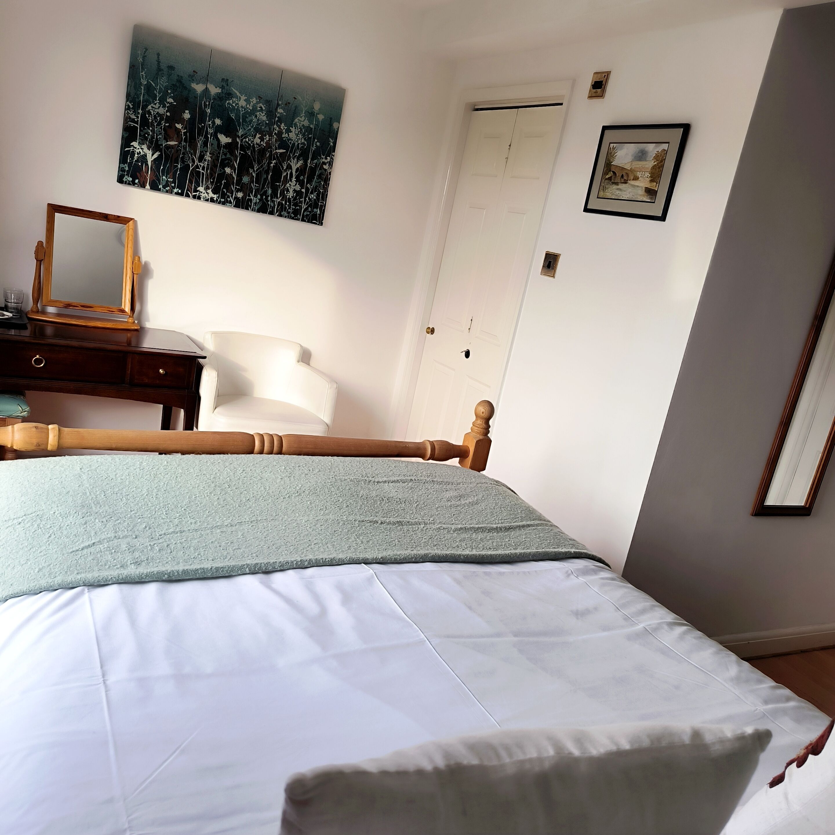 A bedroom with a bed, a wooden headboard, a nightstand, a dresser, a mirror, and a painting on the wall.