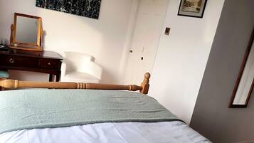 A bedroom with a bed, a wooden headboard, a nightstand, a dresser, a mirror, and a painting on the wall.