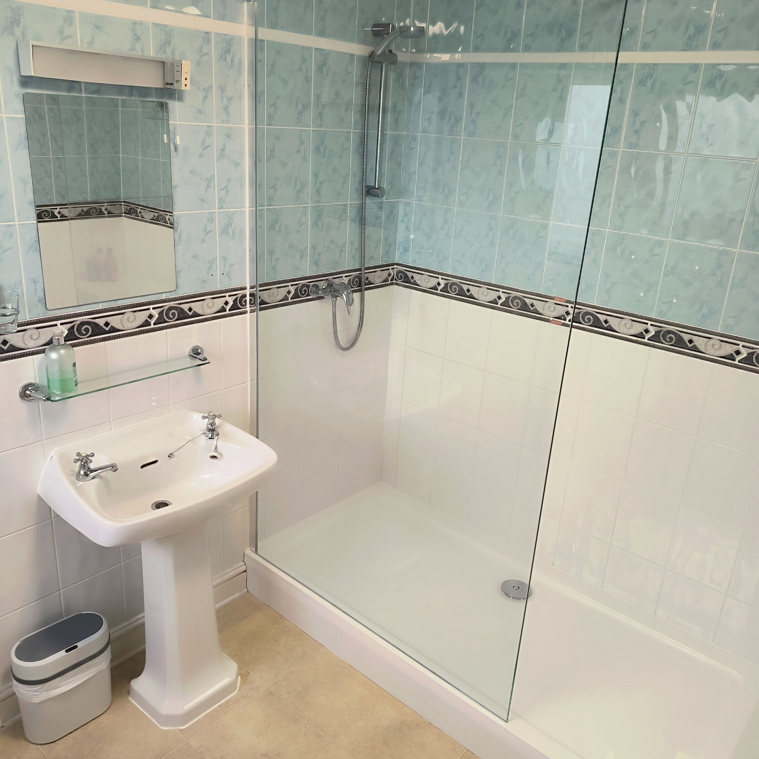A bathroom with a glass-enclosed shower, a white pedestal sink, and a mirror above the sink.