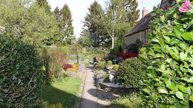 A garden pathway leading to a traditional house with a stone wall and a wooden fence. - Meadow Rise (Cheltenham)