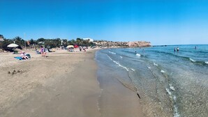 A beach with clear waters, people sunbathing, and a rocky outcrop in the background. - Apartamento 2 Habitaciones Aguilas Junto al mar (Águilas)