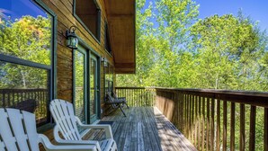 En træterrasse med Adirondack-stole, gelænder og udsigt til træer.
