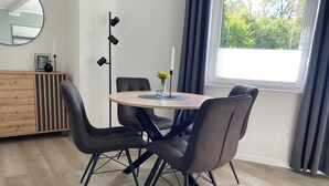 A dining area with a round table and four chairs, a wooden cabinet, and a large window with curtains.