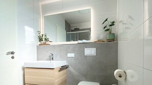 A modern bathroom with a white sink, wooden vanity, a toilet, and a mirror above the sink.