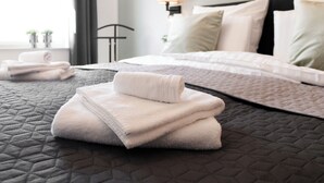 A neatly made bed with a quilted cover, a folded white towel, and a bedside lamp.