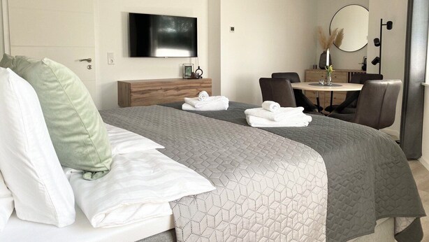 A hotel room with a bed, a desk, a chair, a TV, and a mirror.