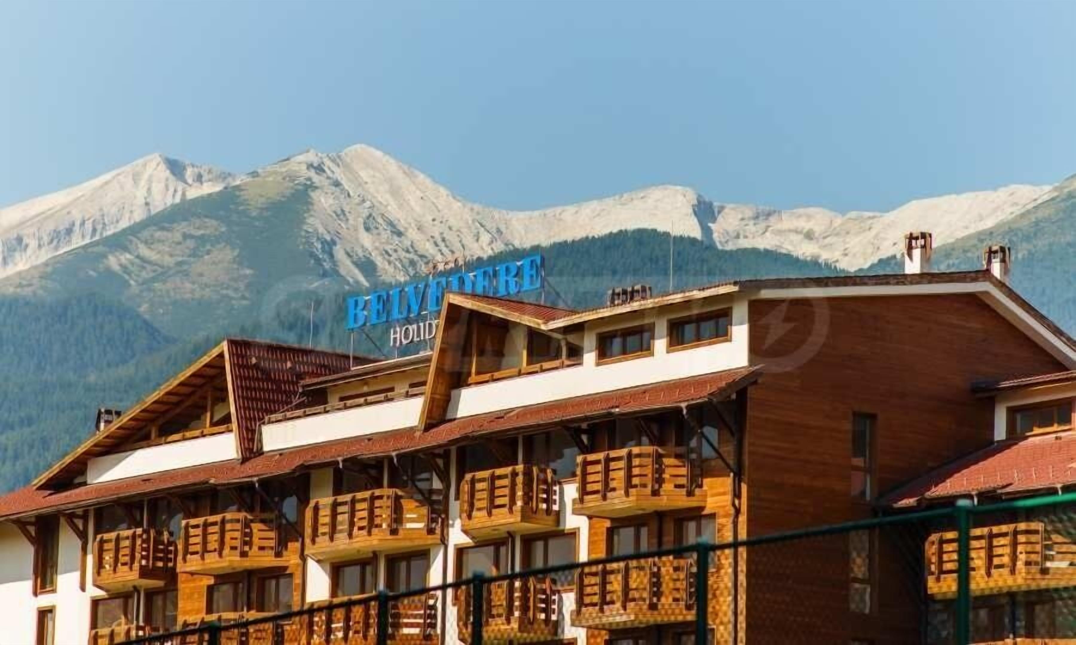 Un hotel con varios balcones y un paisaje montañoso de fondo.
